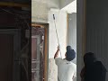 Applying white paint to the building walls and ceiling using a long handled roller tool carefully