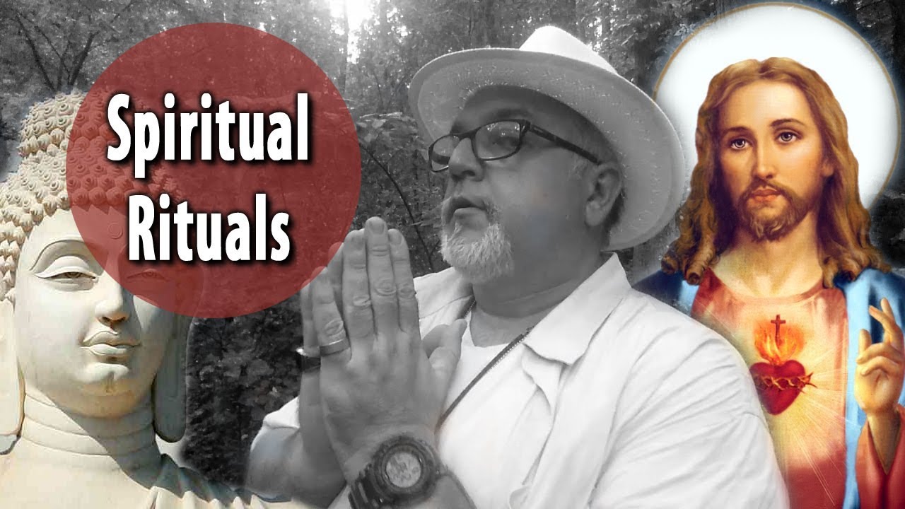  A man wearing a hat and glasses is praying with his hands together in front of a statue of Buddha and an image of Jesus.