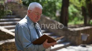 Old Codger Grandpa in Glasses Sits and Reads in a Street in Summer | Stock Footage - Videohive