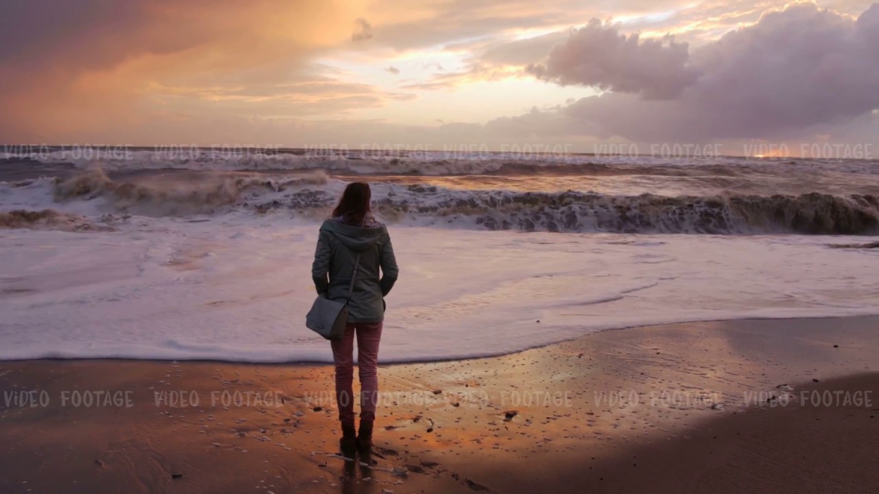 silhouette of a girl. she looks at storm sea in sunset time. waves ...