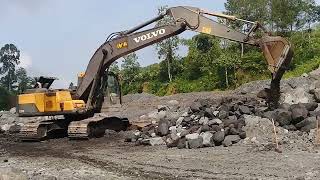 excavator working to collect large rocks in sand mining - mountain slope