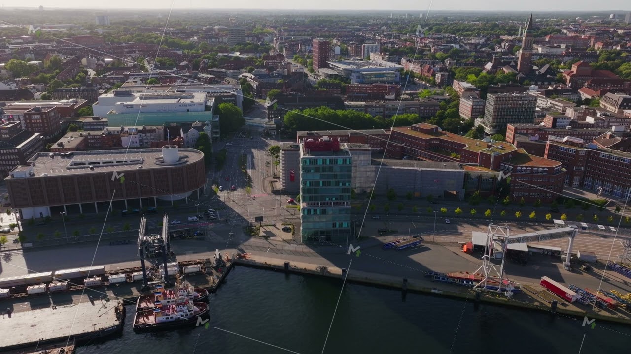 Aerial view of Kiel harbor with cranes loading cargo ships and the surrounding cityscape. Camera