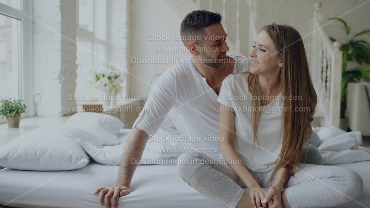 Young beautiful and loving couple embrace and kisisng while sitting on bed after waking up in the