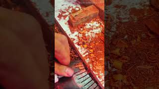 shaping teeth of a wooden comb with a sharp metal chisel tool surrounded by red wood shavings