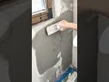 spreading grey cement plaster across the wall surface with a flat metal trowel to create a smooth