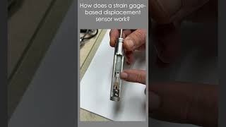 How does a strain gage-based displacement sensor work?