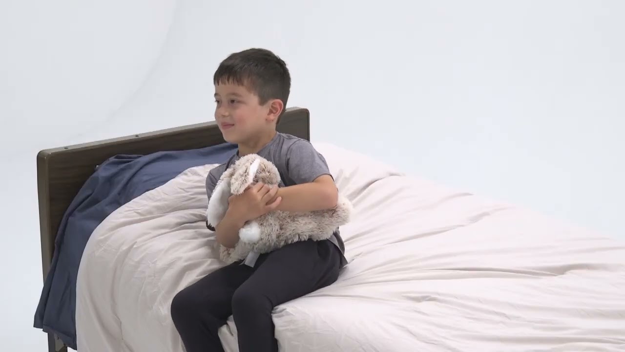A boy sits on a bed holding a stuffed animal while using Medbridge software.