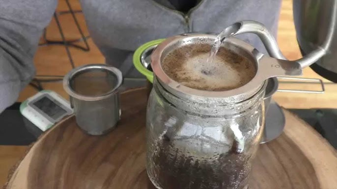 Hot water being poured into a metal tea strainer for brewing coffee, demonstrating the steeping process for can a tea infuser be used for coffee.
