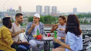 Multiracial group of friends is clinking glasses, drinking soft drinks and eating pizza sitting at screenshot 1