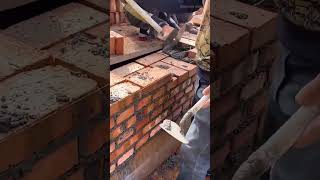 spreading cement mortar on top of brick wall and preparing to place red brick at construction site