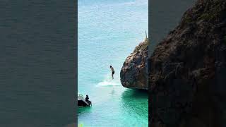 Thrilling Plunge: Daring trio jumping off a cliff into clear emerald waters! #beach #fun #travel