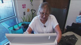 Volunteer seamstress mending clothes of the homeless sits behind her sewing station one last time