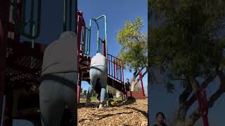 Boy standing on top of jungle gym grabs onto fireman's pole then falls to the ground at playground