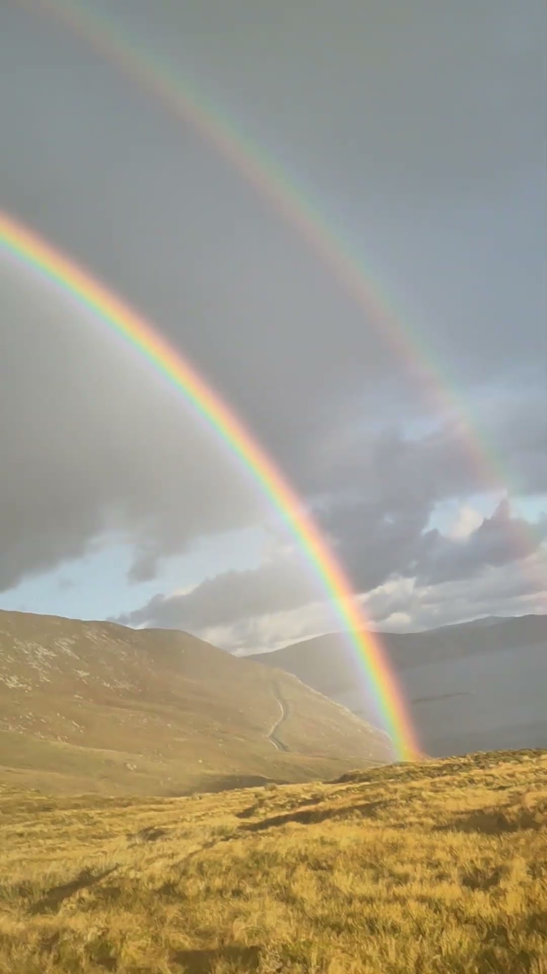 Intense Double Rainbow Forms Against Stunning Mountain Backdrop
