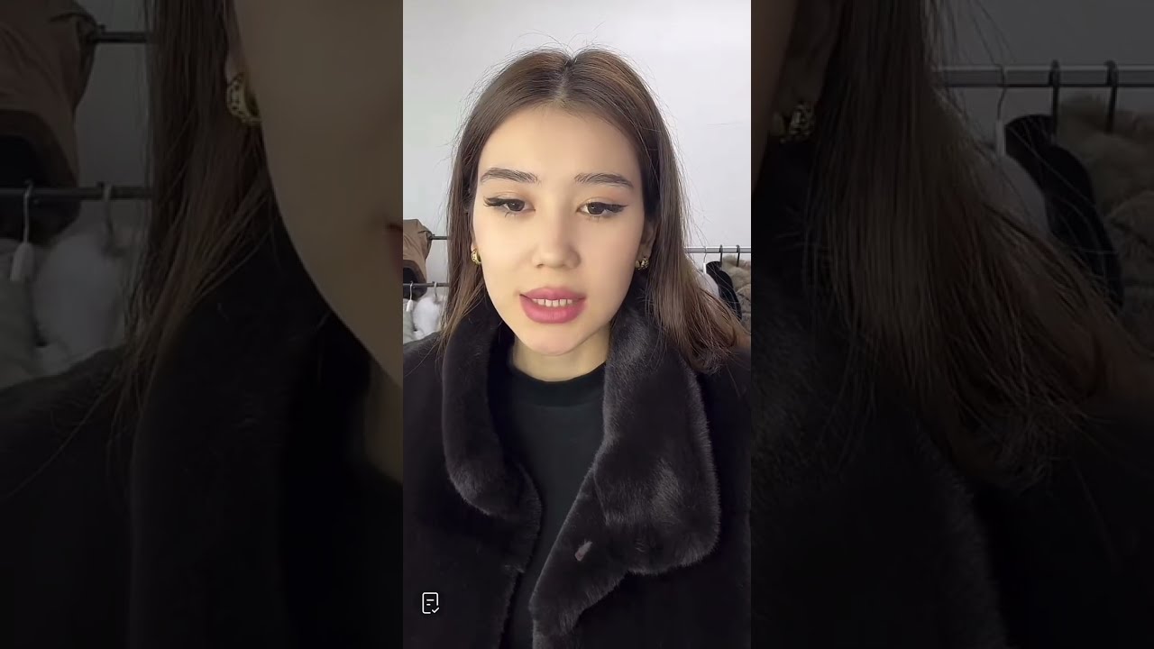 В черном платье и колготках примеряет шубы 