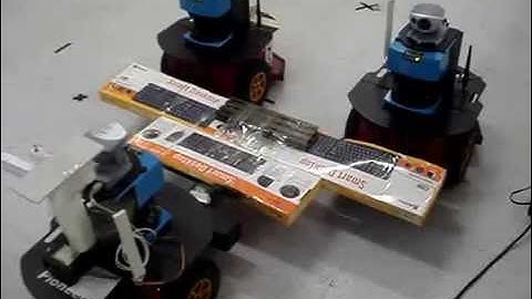Three robots carrying an object over forks in a formation of triangular shape - RealWorld App (HQ)