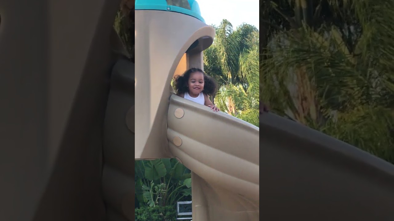 Little girl goes down brown plastic slide at playground then flips over before she gets to the end