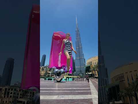 An AR video of a building-sized Barbie stepping out of her box, standing next to the Burj Khalifa.