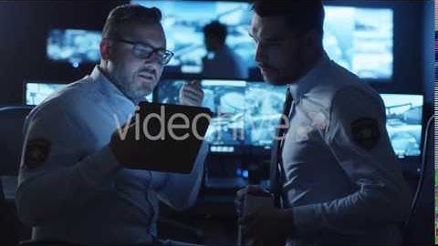 Security Officer Using a Tablet in a Dark Monitoring Room Filled with Display | VideoHive 14742452