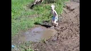 Ребёнок бегает по грязной луже.