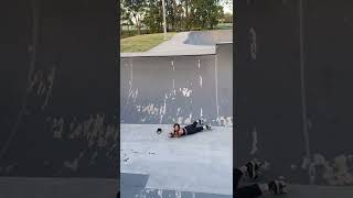 Girl on roller skates rides in bowl at skatepark then grinds spine of ramp and falls bumps forehead