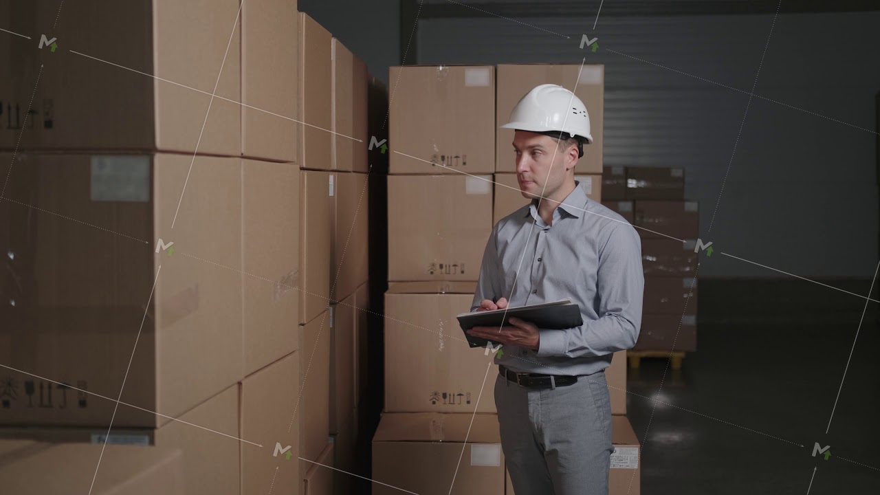 A man works in a warehouse with cardboard boxes, makes an inventory.