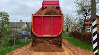 Red dump truck unloading sand for rural road construction and delivery