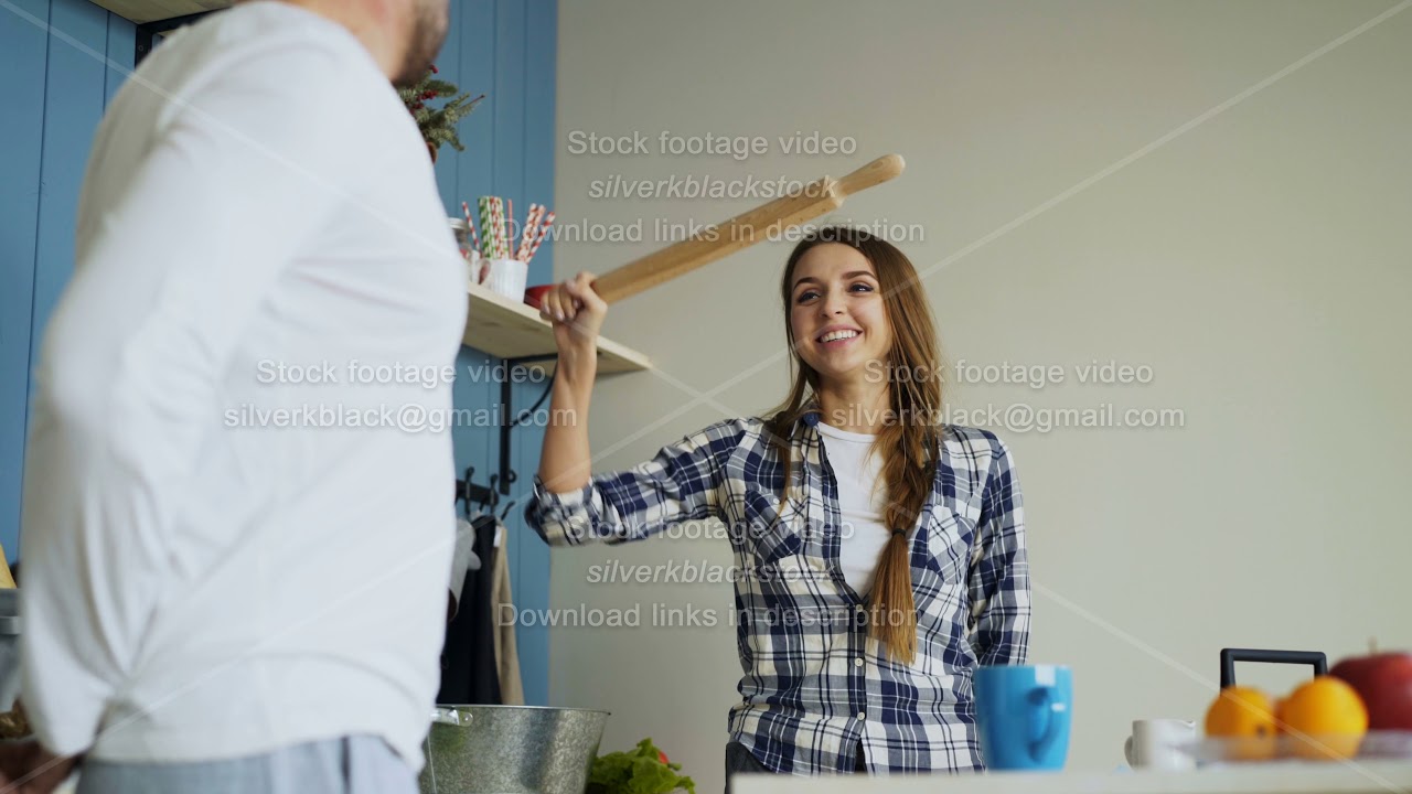 Happy couple having fun in the kitchen fighting with ladle and rolling ...