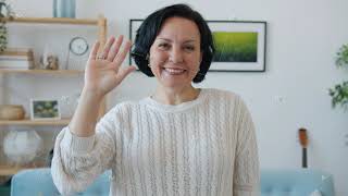 Slow motion portrait of cheerful woman waving hand and smiling standing indoors at home