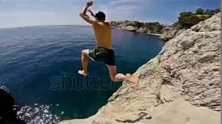 Athletic Young Man Jumping From Cliff Into Ocean Sea Water