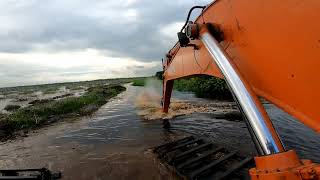 Beko besar alat berat amphibious excavator normalisasi sungai alam di pinggir jalan lintas timur