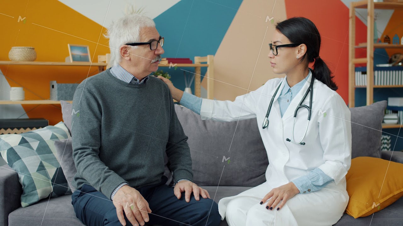 Young woman medic talking to old man touching his shoulder in apartment