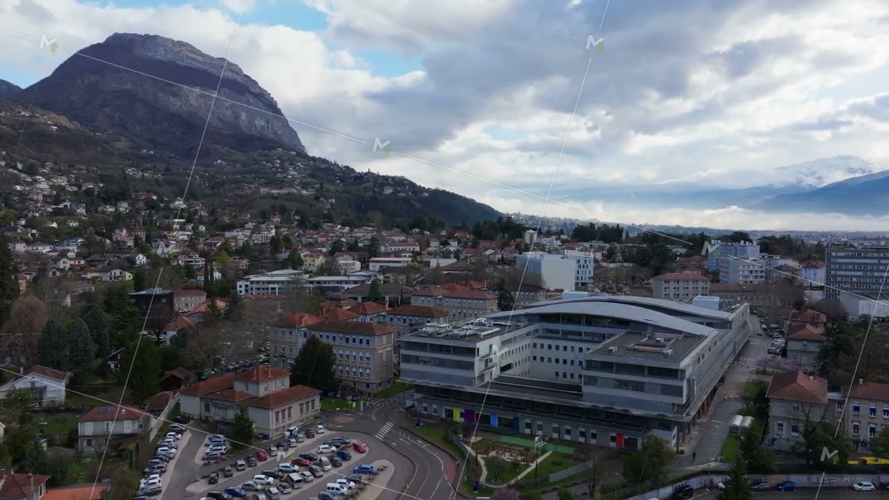 Aerial view of Grenoble cityscape featuring a modern building, parking lot and the Bastille mountain