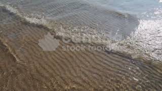 Slow motion sunlit lake water and wave with rippled sand pattern below stock video. HD video.