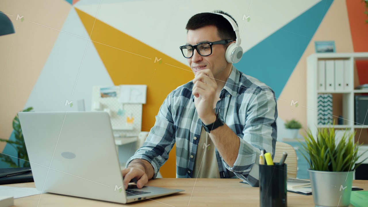 Young man in headphones working with laptop in office and listening to