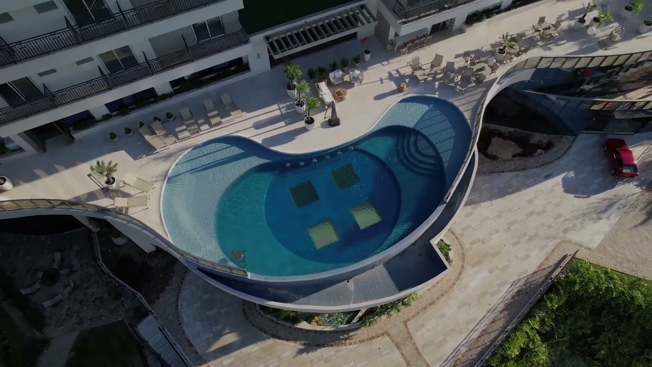 Vista aérea de piscina de formato orgânico com deck, prainha e área de lazer projetada pela Ramiro Piscinas em Rio do Sul, Santa Catarina