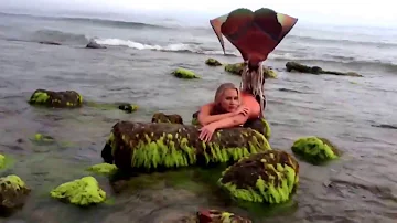 Real life mermaid on rocky shore beach