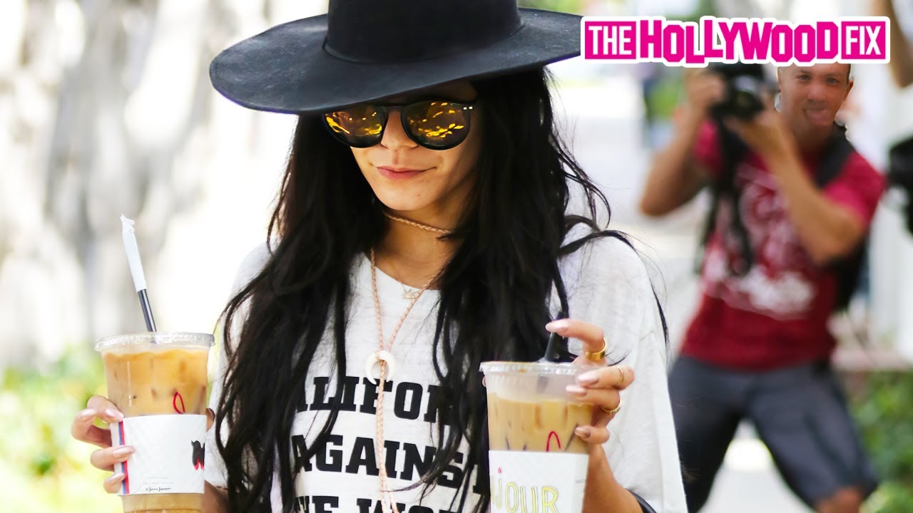 Ванесса Хадженс держит две огромные чашки кофе со льдом и щеголяет в огромной черной шляпе во вре...