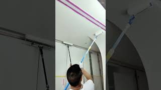 Coating the high white ceiling surface with a long paint roller tool for a neat renovation finish