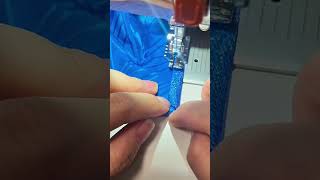 Fingers guide glittery blue trim under sewing machine foot