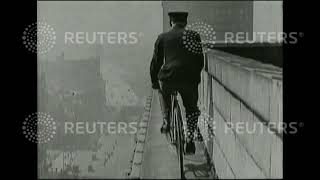 1920 Man rides bicycle on ledge of building