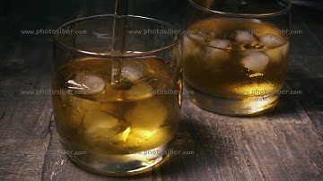 Slow motion in one of the glasses with ice pour whiskey