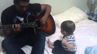 Un bébé rit en regardant son père jouer de la guitare