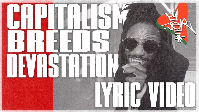The image features bold text stating "CAPITALISM BREEDS DEVASTATION" and "LYRIC VIDEO," alongside a smiling artist wearing sunglasses and gesturing expressively. The background includes a mix of colors, emphasizing the message.
