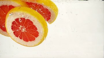Grapefruit orange slices fall into water with splashes and bubbles, slow motion close-up