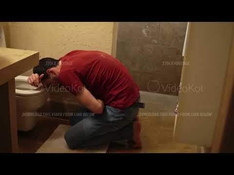 Man is leaning over toilet and vomiting then wiping mouth with paper sitting in lavatory