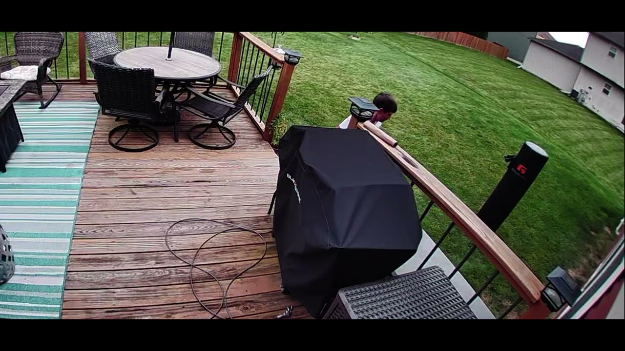 Boy attempts to jump onto punching bag from backyard deck and lands on grass Security camera