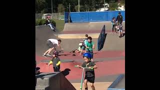 Skateboarder does trick at skate park and crashes into a scooter kid