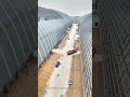 Workers are installing the exterior wall panels onto the massive arched steel framework