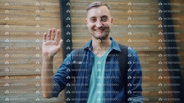 Slow motion of friendly handsome guy waving hand smiling outdoors in the street